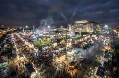 Aerial nighttime view of the Houston Rodeo carnival grounds at NRG Park, with colorful rides and a large crowd.